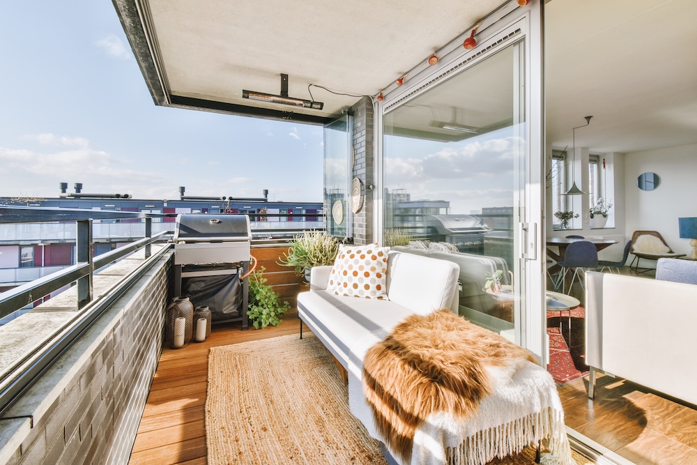 balkon ze strefą wypoczynkową i do grillowania balkon z jasną sofą pod oknem i grillem w rogu