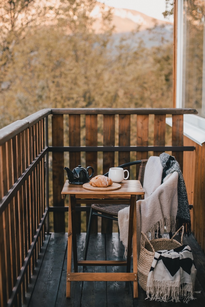 balkon z drewnianą balustradą i krzesłem ze stolikiem balkon z drewnianym stolikiem i fotelem okrytym pledem